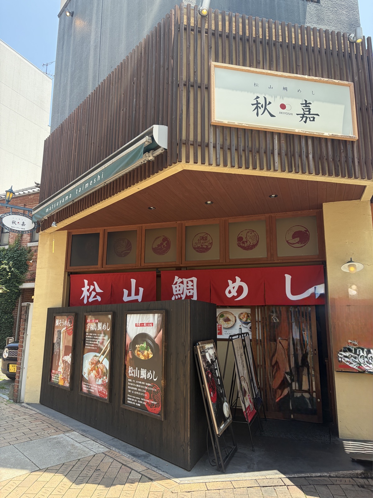 松山城ロープウェイ街にある松山鯛めし秋嘉の外観。赤い暖簾と看板