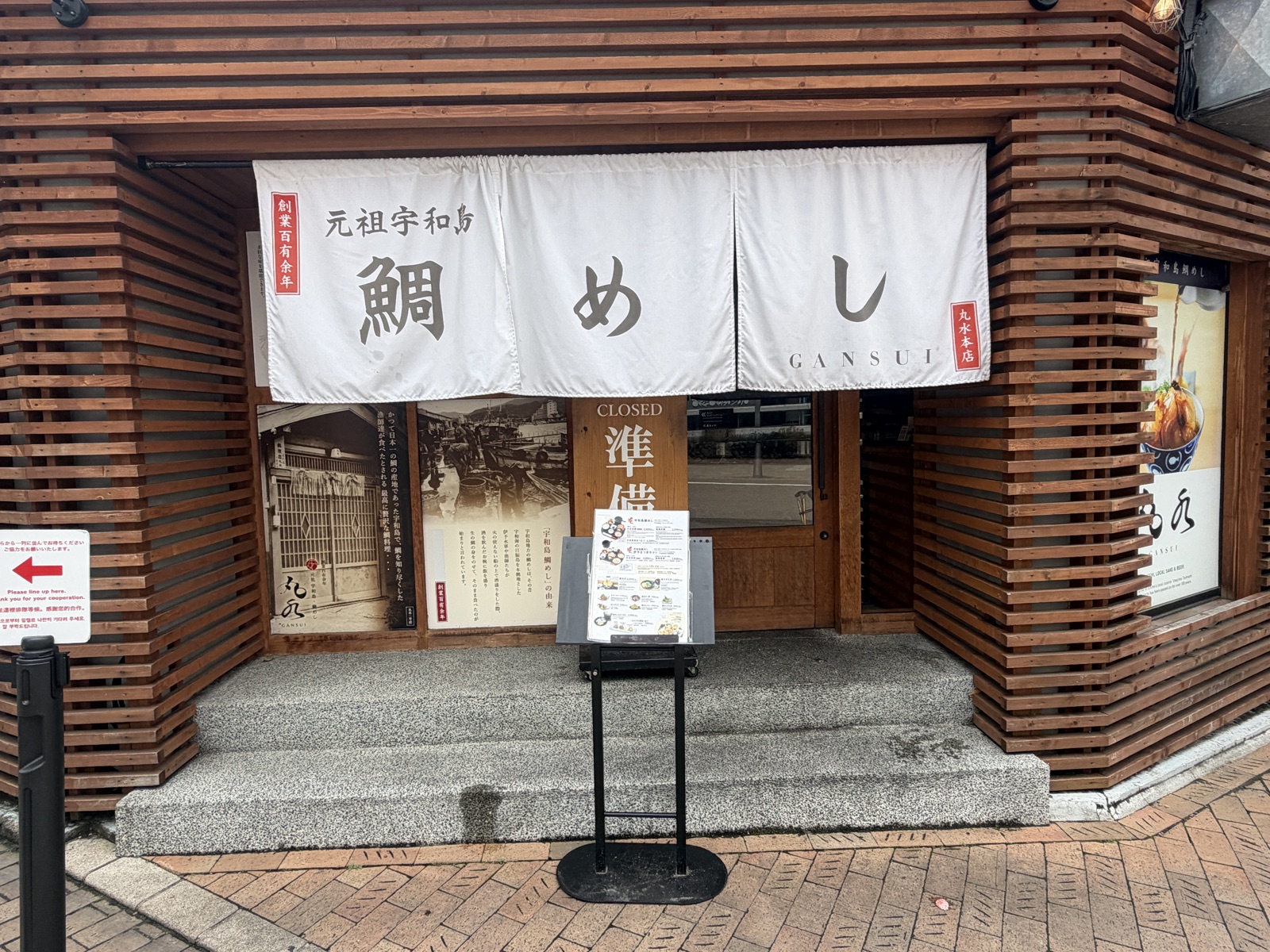 松山城ロープウェイ街にある元祖宇和島鯛めし丸水の外観。白い暖簾と創業百余年の文字