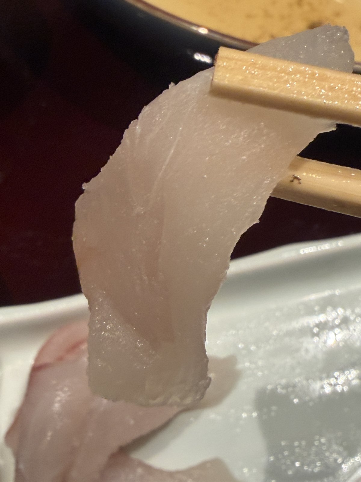 箸で持ち上げたあいごのお刺身。白く透き通った身