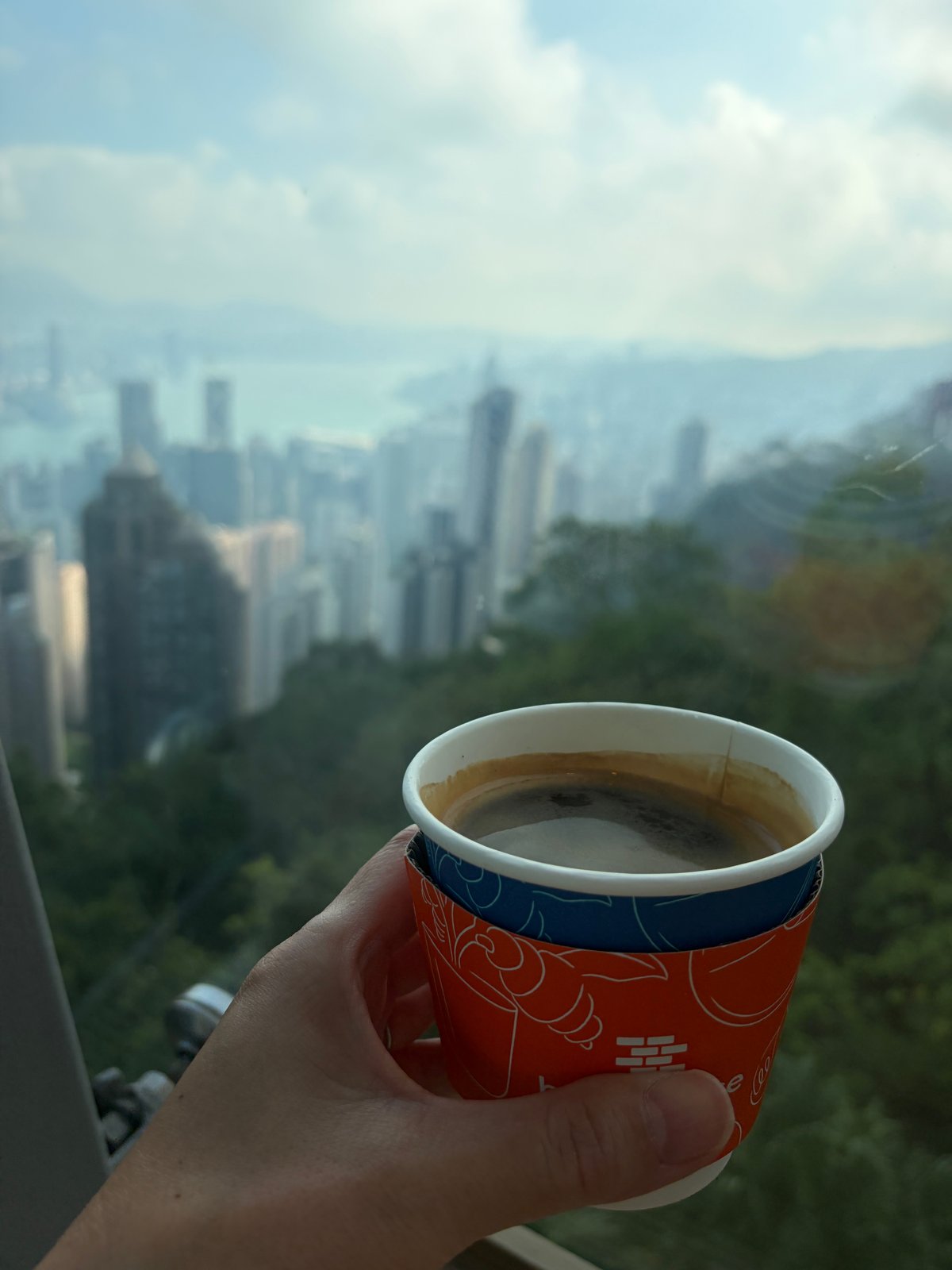 香港の景色を背に、手に持ったアメリカーノのカップ