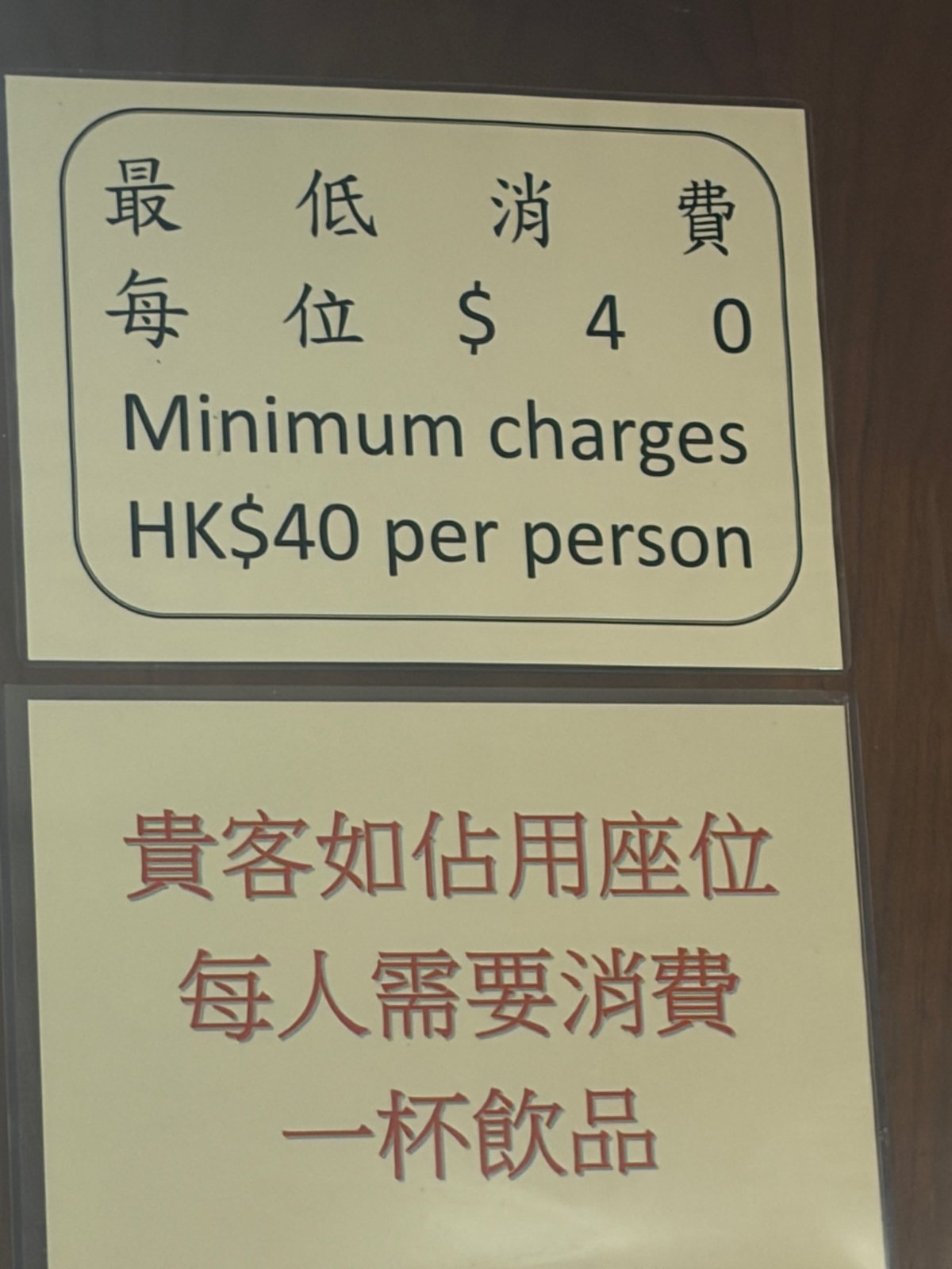 壁の貼り紙。「最低消費 毎位$40 Minimum charges HK$40 per person」と、その下に「貴客如佔用座位 每人需要消費一杯飲品」