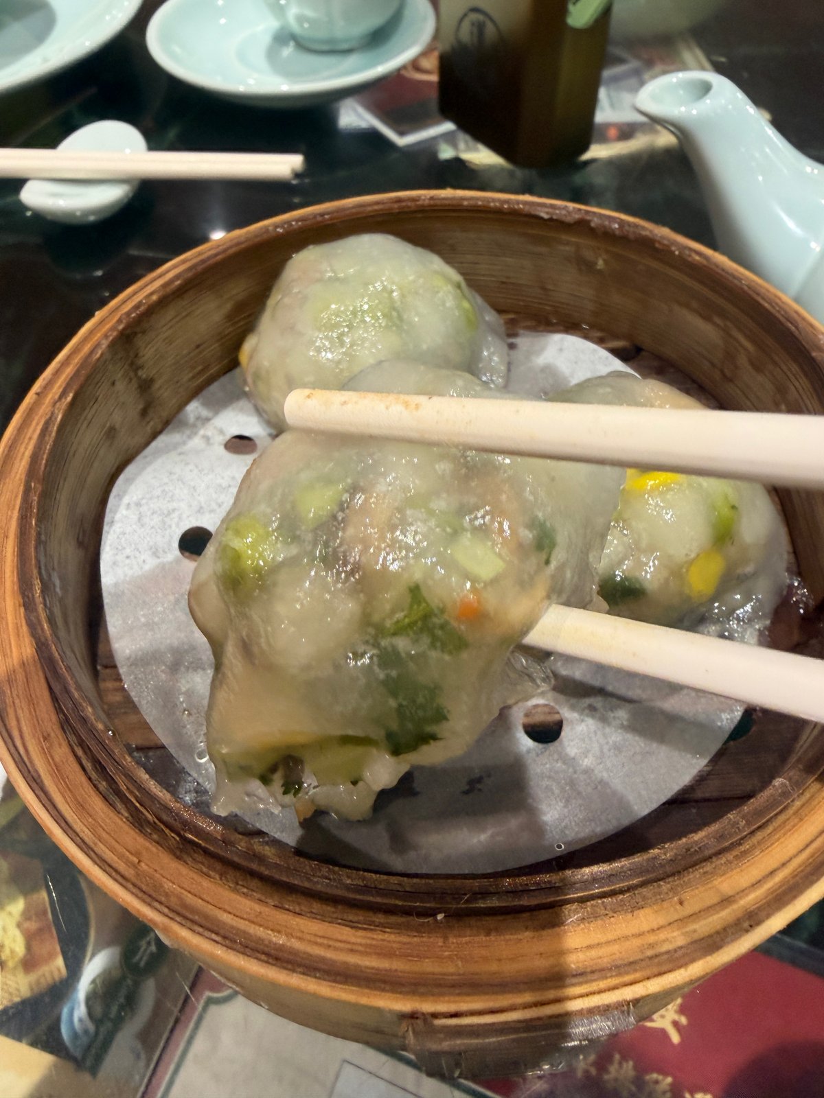 箸で持ち上げた蒸し餃子。中に緑の野菜やコーンが見える