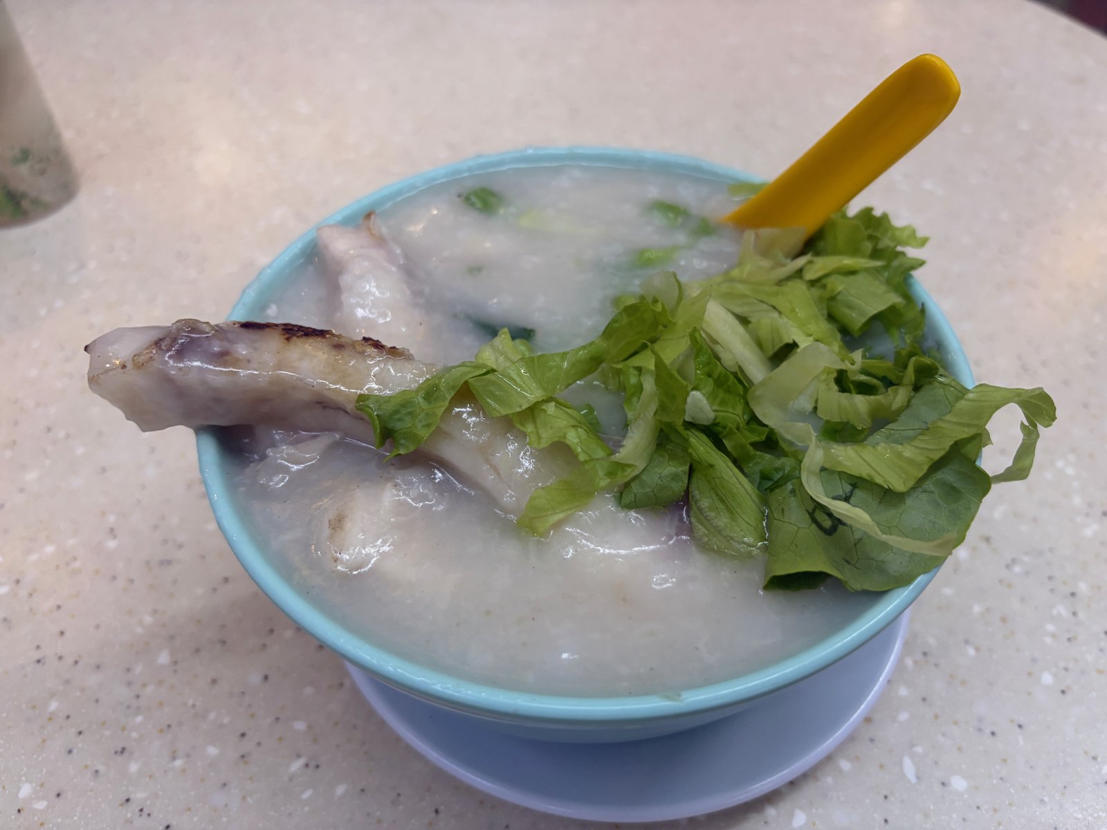 お椀から焼き色のついた魚がはみ出した魚腩粥。上にレタスがのっている