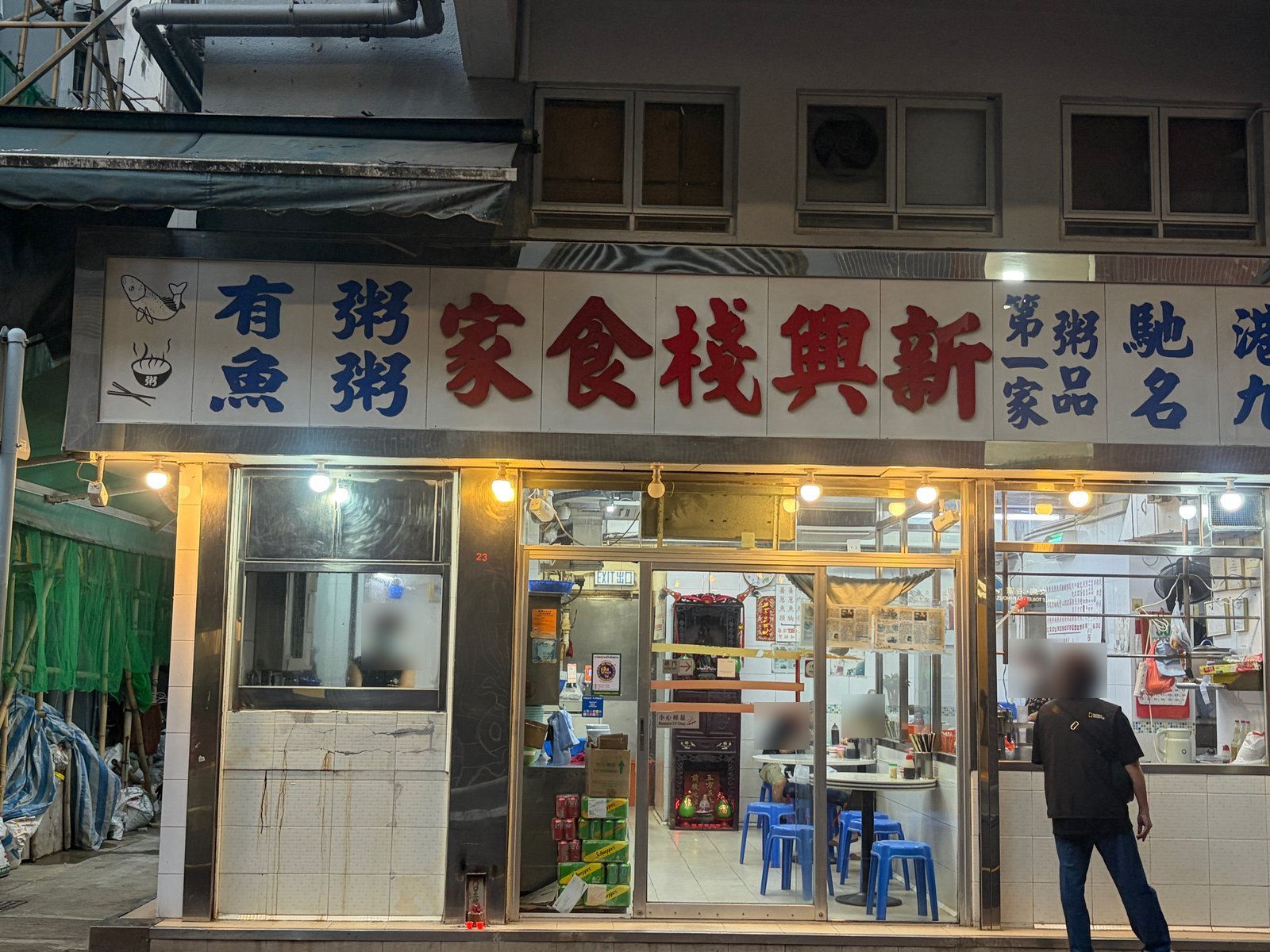 白い看板に赤い文字で「新興棧食家」、青い文字で「有魚粥」「粥粥」。夜の店先に明かりがついている